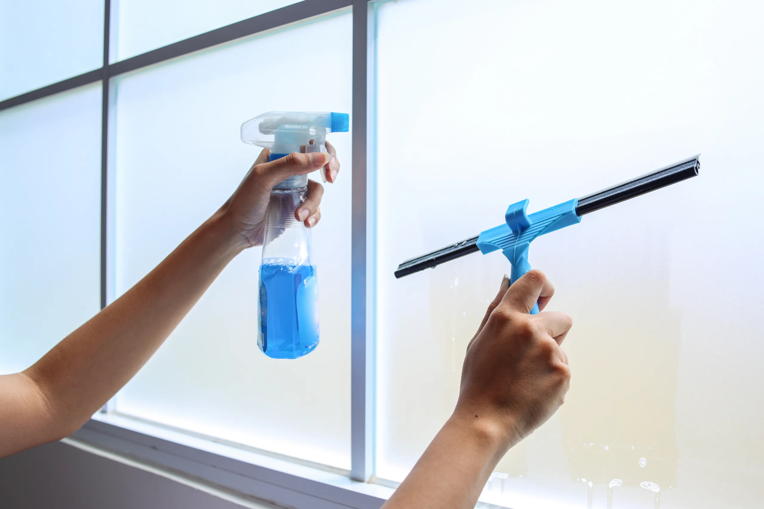 Fensterreinigung in Kiel: Scheibe wird mit Sprühflasche und Abzieher gereinigt